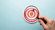 © Nur - Close Up of Goal Achievement with Target on Hand and Magnifying Glass Focusing on Success with Precision Accuracy and Detail