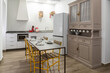 © Manuel - Clean interior of a contemporary kitchen and dining space featuring white cabinets, a table, and a classic hutch