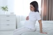 © New Africa - Pregnant woman suffering from pain on bed in bedroom, space for text
