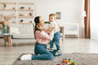 © Prostock-studio - Pretty young mother enjoying time with her adorable toddler son at home, playing with kid boy in living room, sitting on floor carpet, copy space
