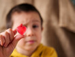 © light - Close-up of a young boy examining a pink heart-shaped jelly candy. A pensive child holds a gummy sweet up to eye level with a focused, questioning expression, illustrating curiosity, sensory