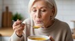 © Running opossum - elderly woman enjoying hot soup at home kitchen, feeling cozy and warm on winter day