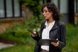 © Studio Sincère/Stocksy - Woman engaged with phone while holding documents outdoors