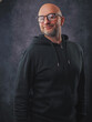© mark_gusev - A man wearing a black hoodie and glasses is smiling. He is standing in front of a grey background. Classic portrait of a confident and friendly looking male model.