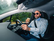 © mark_gusev - Bald man with grey beard is a car driver. Male in light blue shirt and dark glasses holding a brown cup with coffee, forest background. Transportation industry. Drinking energy drinks to stay awake.