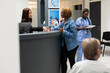 © DC Studio - Friendly receptionist at front desk assists patient with updating health records and scheduling treatment visits in clinic. Asian female administrator guiding woman with hospital registration forms.