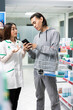 © DC Studio - Male customer uses cellphone to read detailed medicine instructions while consulting drugstore attendant. Asian man asks female pharmacist for assistance in choosing the right product in pharmacy.