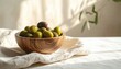 © Jasan - Close up shot of a wooden bowl filled with fresh green and black olives on a textured white cloth with soft natural light and blurred green foliage in the background.