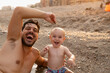 © Raul Navarro/Stocksy - Father and son laughing together on beach during sunset