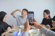 © Gatot - Hands Holding Smartphone Recording Happy Young Muslim Man Eating During Eid Family Gathering