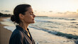 © Hanna - Woman stands on beach with eyes closed and enjoys sunset by the ocean in a peaceful moment on a warm evening