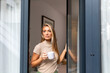 © Graphicroyalty - Beautiful young woman standing by balcony door holding cup of coffee. Female looking out window while enjoying morning beverage at home. Relaxation, domestic lifestyle and peaceful mood concept.