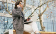 © olezzo - Mature business woman with laptop putting in wireless earbud for video call on a city bench