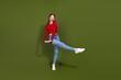 © deagreez - Young woman dancing in a red top jeans and white sneakers against a green background for lifestyle fashion stock photo