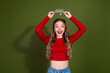 © deagreez - Young blonde teen girl in red top holds crown above head smiling against green background