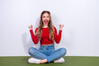 © deagreez - Young woman in red top and jeans sits cross legged on floor smiling with fists up in celebration