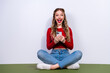 © deagreez - Young woman in red top sits cross legged smiling at her phone indoors