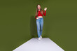 © deagreez - Young woman in red crop top and jeans waves hello on a green studio backdrop for fashion lifestyle advertising and shopping campaign