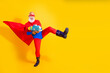 © deagreez - Bearded senior superhero in bright red cape and blue suit performs a high kick with toy gun against a yellow background for a playful festive image
