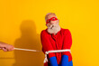 © deagreez - Senior bearded man in red superhero costume tied with rope against bright yellow background creating playful dramatic scene