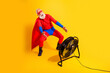© deagreez - Senior superhero in red and blue costume dances in front of a large fan against a bright yellow backdrop