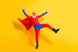 © deagreez - Senior superhero in bright red blue costume performs a playful jump against a yellow backdrop