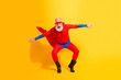 © deagreez - Energetic senior superhero performs dynamic jump in bright yellow studio wearing red suit cape and mask for fun