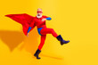 © deagreez - Dynamic senior superhero leaps in bright red costume with cape against yellow background for fun holiday show and upbeat promotion