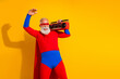 © deagreez - Energetic elderly superhero man in red and blue costume with cape dancing and posing with a boombox against a bright yellow background for stock listing