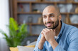 © Liubomir - Content bald man in a blue shirt smiling and looking away, daydreaming and contemplating future plans in a relaxed, comfortable home setting with warm, hopeful expression