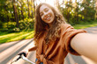 © maxbelchenko - A happy woman with a phone and a bicycle in a sunny park. A beautiful woman rides a bicycle, blogs, and enjoys the sunset. Blogging, weekend concept.
