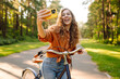 © maxbelchenko - A happy woman with a phone and a bicycle in a sunny park. A beautiful woman rides a bicycle, blogs, and enjoys the sunset. Blogging, weekend concept.