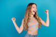 © deagreez - Young woman cheers with raised fists against blue background