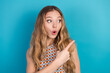 © deagreez - Young woman with surprised expression pointing to the right against blue background