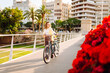 © maxbelchenko - A smiling woman with a bicycle enjoys a sunny day in the city. A beautiful woman rides a bicycle among bright flowers. Relaxation concept, weekend. Active lifestyle.