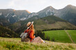 © maxbelchenko - Female traveler with a backpack and hat walks along a trail among green hills. The young woman enjoys the mountain scenery, feeling the freedom of adventure. The concept of freedom, enjoyment.