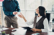 © deagreez - Business discussion in a modern office a woman in a vest hands a cup to a colleague standing beside a desk