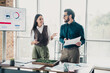 © deagreez - Two professionals discuss business strategy in modern loft office with charts and plants