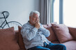 © Daniel - An elderly man sits on a sofa at home holding his cheek in pain, suffering from a toothache and showing discomfort while dealing with dental problems in a quiet living room setting