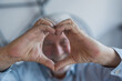© Daniel - An elderly man sits on a sofa at home holding his hands over his heart with affection, expressing love and emotional warmth while enjoying meaningful bonding moments with his family