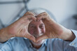 © Daniel - Elderly man sits on a sofa holding his hands to his heart in affection. He enjoys bonding moments with family, feeling warmth and togetherness.