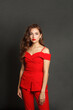© artmim - Attractive young woman in red suit standing against black studio wall background