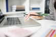 © Pattra - A woman in a gray suit is sitting at a desk with a laptop and a presentation. She is smiling and holding a piece of paper. Concept of professionalism and confidence