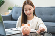 © KMPZZZ - Financial, asian young woman, girl putting stack coins on table for calculate cost sitting in living room at home, financial plans to spend enough money on his income for saving money and payment.
