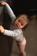 © Yaraslava - curious toddler reaching and leaning on a dark kitchen cabinet countertop in soft warm light, candid domestic portrait highlighting skin tones, muted browns and pinks, playful intimate expression