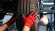© Rymma - Automotive mechanic hands in red protective gloves checking car tire tread on lifted vehicle in modern service garage, professional auto repair maintenance inspection safety transport industry concept