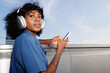 © Artem Podrez/Stocksy - Portrait Woman Holding Phone with Headphones  Sky Background