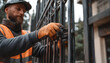 © Prasanth - A construction worker in a safety vest and gloves installs a metal gate on the property, and his hands carefully fix the gate bars. He works on outdoor buildings with precision and skill.