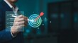 © Ada - Business goal setting concept with businessman using digital stylus to target center of dartboard Represents Business Goal Achievement and Strategy
