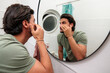 © DusanJelicic - Young man examining his face in a bathroom mirror, practicing a skincare and grooming routine at home, focused on appearance, hygiene and everyday self care